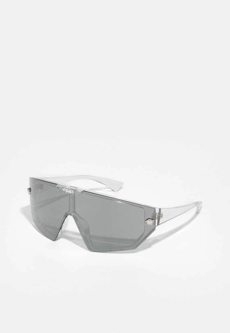 Grey oversized sunglasses with a hexagonal lens shape, clear plastic frame, and silver accents on the sides featuring a logo detail.