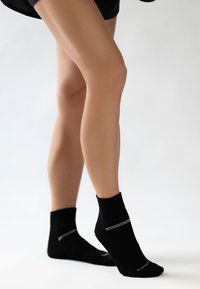 Schwarze Knöchel-Socken aus weichem Material, mit einem gerippten Bündchen und einem weißen horizontalen Streifen. Entwickelt für Komfort und Passform.