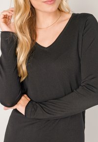 Black long-sleeve top with a V-neck design and ribbed texture. Lightweight fabric with a soft finish, featuring fitted sleeves and a casual fit.