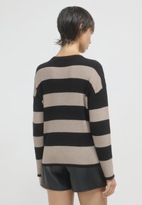 Gestreifter Pullover in Schwarz und Beige mit geripptem Struktur, Rundhalsausschnitt und lockerer Passform. Getragen mit schwarzen Shorts, Rückansicht gezeigt.
