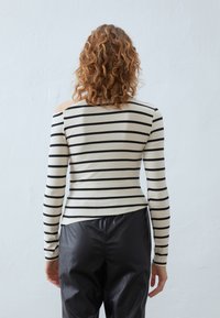 Svart og beige stripete langermet topp med off-the-shoulder design. Mykt strikket materiale. Kombinert med høyhælte svarte bukser.