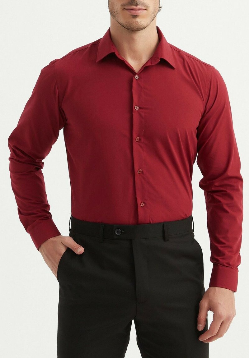 Chemise rouge à manches longues avec un col classique, en tissu lisse et coupe ajustée, associée à un pantalon noir.