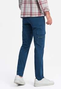 Pantaloni cargo blu con vestibilità slim, dotati di tasche laterali e cerniere, realizzati in misto cotone, abbinati a sneaker bianche.