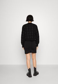 Pull cropped noir avec des motifs verticaux texturés et des embellissements roses, associé à une jupe noire froncée et des bottes noires chunky.