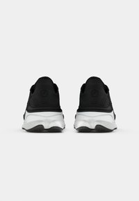 Scarpe da ginnastica nere con tomaia in tessuto strutturato, suola intermedia bianca curvata e suola in gomma. Presentano dettagli del logo sul tallone.