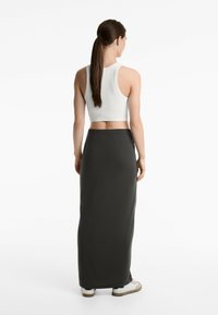 Gonna nera lunga con vita elastica, abbinata a un crop top bianco a coste. Il modello ha i capelli lunghi e si trova in piedi su uno sfondo neutro.