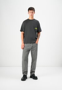 Dark gray cotton t-shirt with short sleeves and a small neon yellow graphic. Paired with light gray denim jeans and black chunky shoes.