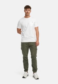 T-shirt bianco in cotone con maniche corte e taschino sul petto, abbinato a pantaloni cargo verde oliva con tasche laterali e orli risvoltati.