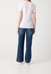 T-shirt blanc à manches courtes associé à un jean évasé bleu avec poches arrière et ourlet brut, complété par des baskets blanches.