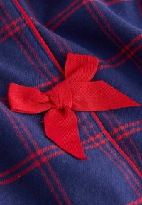 Námořnická modrá látka s kostkovaným vzorem v červené barvě. Vyznačuje se výrazným červeným mašlí, vyrobeným z texturované stuhy.