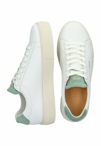 Weiße Leder-Sneaker mit einem mintgrünen Wildlederakzent an der Ferse. Flache Schnürsenkel und eine strukturierte Gummisohle. Markenname auf der Zunge geprägt.