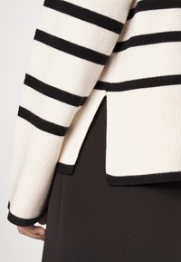 Sweter z dzianiny w czarno-białe poziome paski, z prążkowanymi mankietami, rozciętym dołem i miękką teksturą. Czarne materiały pod spodem.