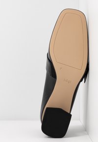 Chaussure en cuir noir avec une finition lisse, bout arrondi et semelle en caoutchouc noir texturé. Présente une semelle extérieure beige avec un logo en relief.
