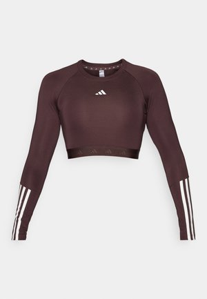 Korte top van donkerbruin stof met lange mouwen. Voorzien van het witte Adidas-logo en drie witte strepen op elke mouw. Gladde textuur.