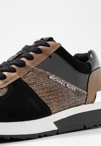 Zapatillas altas en negro y marrón con detalles de ante, cuero y metálicos; presentan un lateral texturizado y estampado y una suela de goma blanca.