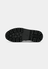 Semelle de chaussure en caoutchouc noir rugueuse avec des rainures profondes et des motifs circulaires et rectangulaires pour la traction sur un fond clair uni.