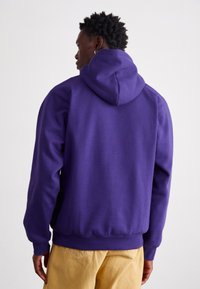 Paarse hoodie met een voorzak, ribgebreide manchetten en zoom. Glad, casual stofafwerking, gedragen boven een beige broek.