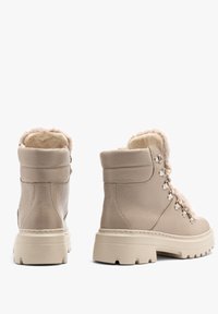 Beżowe skórzane botki za kostkę z sztucznym futerkiem, okrągłym noskiem i metalowymi oczkami z sznurówkami. Gruba podeszwa o teksturowanym wzorze.