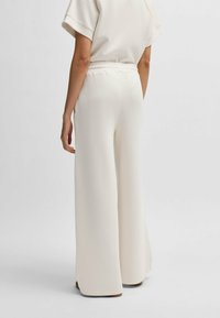 Lightweight, cream-colored wide-leg trousers with an elastic waistband and smooth texture, featuring a clean, minimalist design.