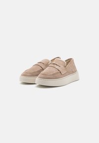 Beige semskede slip-on sko med rund tå, doble elastiske stropper og tykk hvit gummisåle. Myk fôr synlig inni.