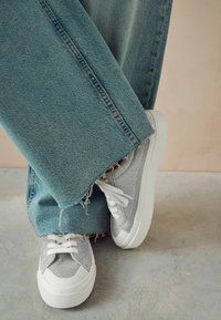 Silver mesh låga sneakers med vita sulor, matchade med vida denimjeans, nötta i fållen, mot en mjuk, dämpad bakgrund.