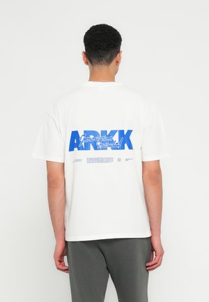 Weißes Baumwoll-T-Shirt mit kurzen Ärmeln, auf der Rückseite mit großen blauen Buchstaben bedruckt, die "ARKK" und "Innovation Included" lesen.