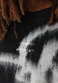 Pull en polaire noir et blanc avec un large motif abstrait et un petit logo blanc, mettant en avant un tissu doux et texturé.