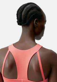 Koral sportstopp med utskjæringsdesign på ryggen, som fremhever glatt, elastisk stoff. Håret stylet i pene fletter.
