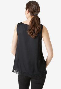 Svart ärmlös topp i ett smidigt material, med spetsdetaljer vid fållen. Baksidan är något längre, med rundad halsringning.