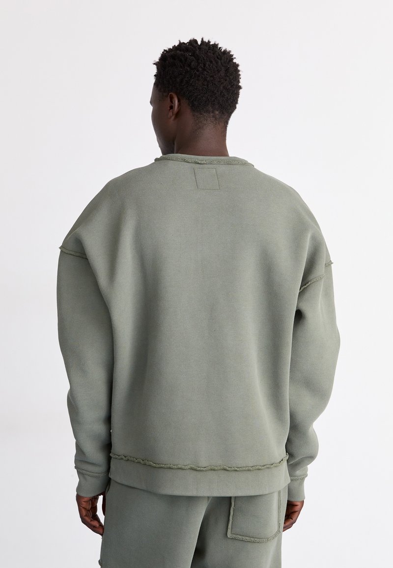 Übergroßer grüner sweatshirt mit weicher Textur, rohem Saum und gerippten Bündchen. Verfügt über ein Rückenpatch-Detail und ein lockeres Fit-Design.