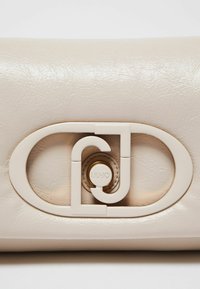Creme læder håndtaske med en glat tekstur, rektangulær form og en fremtrædende oval logo spænde med gulddetaljer.