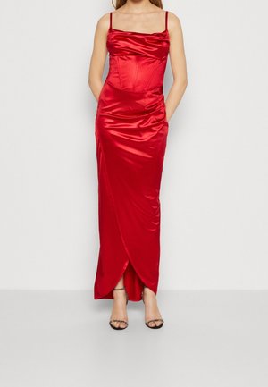Femme portant une robe sans manches en satin rouge brillant avec des fines bretelles et un ourlet style tulipe, assortie à des talons ouverts noirs.