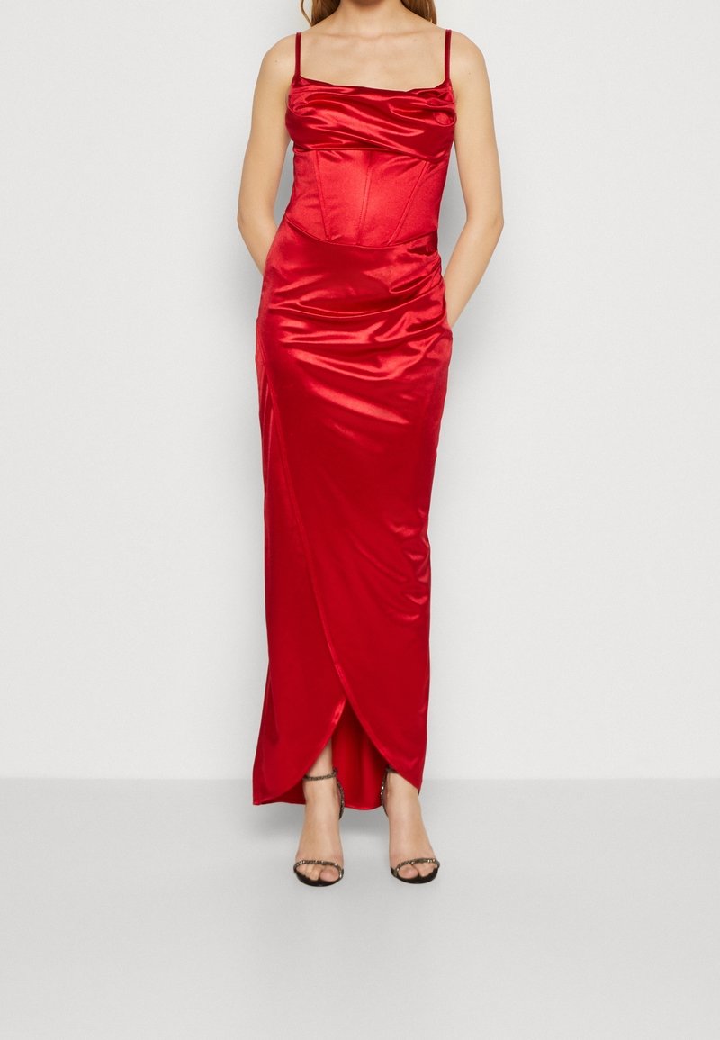 Femme portant une robe sans manches en satin rouge brillant avec des fines bretelles et un ourlet style tulipe, assortie à des talons ouverts noirs.