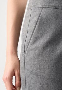 Jupe crayon en tissu gris présentant une silhouette épurée, une texture subtile et des poches latérales, avec une couture soignée le long des coutures.