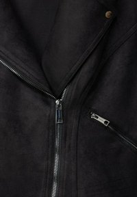 Svart faux suede-jacka med slagkrage, som har silverfärgade dragkedjor framtill och i fickorna, med en slät textur och minimalistisk design.