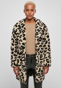Kaput najbolja s leopard uzorkom, u krem i crnoj boji; ima široki ovratnik, duge rukave i ležeran kroj. Nosi se preko bež rebrastog topa.