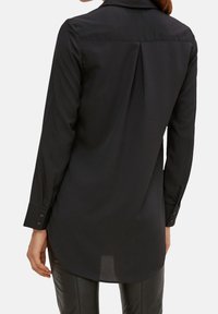 Schwarzes Langarmshirt mit glatter Textur, ausgestattet mit einer Rückenfalte, geknöpften Manschetten und einem abgerundeten Saum.