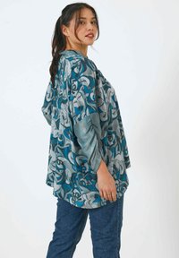 Loose-fitting blouse featuring an abstract blue and gray pattern, with long sleeves and a rounded hem, made from lightweight fabric.
