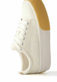 Biały sneakers na platformie z koronkowym sznurowaniem, z delikatną kwiatową fakturą i grubą beżową gumową podeszwą, widziany z boku.