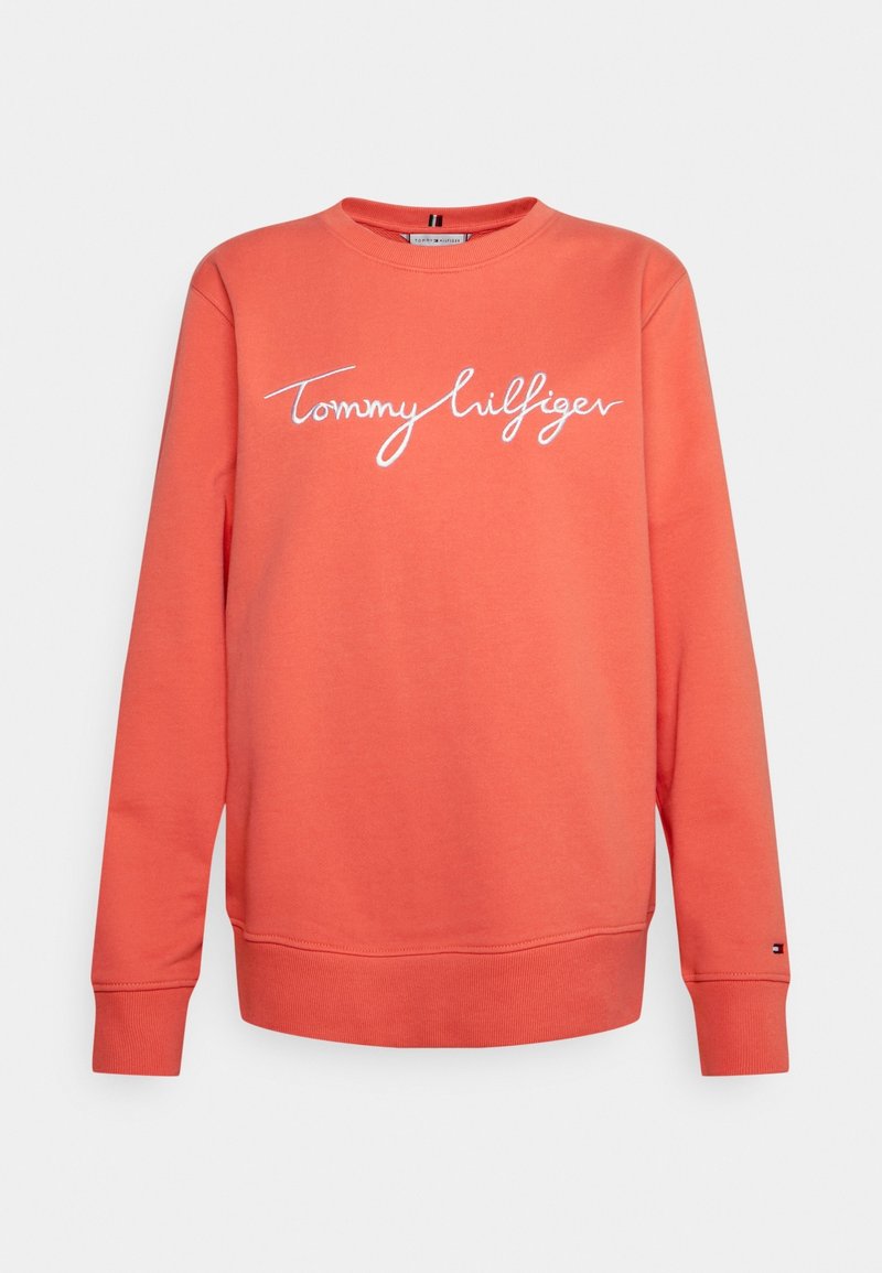 Sweat-shirt corail à manches longues avec col rond, inscription blanche "Tommy Hilfiger" sur la poitrine et petit logo sur le poignet gauche.