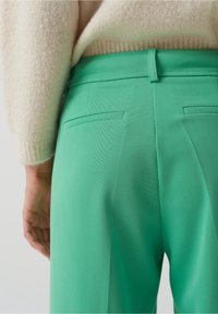 Gröna skräddarsydda byxor med en slät textur, med två bakfickor och en åtsittande midja, kombinerade med en krämfärgad tröja.