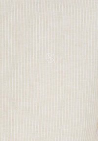 Tessuto beige con righe bianche verticali, che presenta un sottile logo al centro. La texture sembra liscia e leggera.