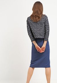 Mörkblå tajt blyertskjol med två framfickor, kombinerad med en texturerad, kort svart och vit tröja med trekvartsärmar.