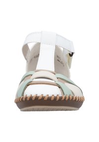 Sandale ouverte blanche et vert pastel avec des brides, présentant un design tissé et des détails de surpiqûres brunes contrastantes autour de la semelle.