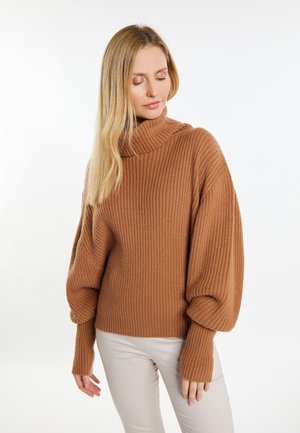 Brauner gerippter Rollkragenpullover mit übergroßen Ärmeln und enganliegenden Bündchen, aus weichem Strickmaterial, kombiniert mit cremefarbenen Hosen.