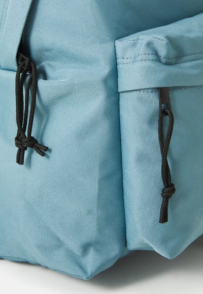 Sac à dos en tissu bleu avec un matériau texturé, équipé de cordons de tirage noirs ajustables et de poches latérales pour le rangement.