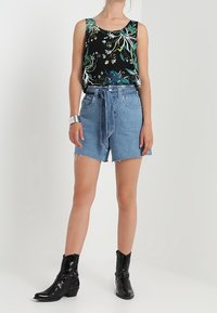 Top senza maniche nero con fantasia floreale, pantaloni di jeans leggeri blu con vita annodata e stivaletti neri alla caviglia. Tessuto morbido, design casual e orlo sfrangiato sui pantaloni.