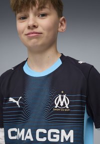 Tumed sinine spordijumper helesiniste aktsentidega; esiküljel on Puma logo, tikitud klubi embleem ja punktmuster.