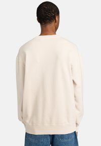 Sudadera color crema con un corte relajado, puños y dobladillo acanalados, y una textura de tela suave. Sin marcas ni patrones visibles.