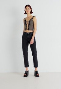 Black lace-up crop top with a textured finish, paired with high-waisted black jeans and chunky heeled sandals. Minimalistic design.